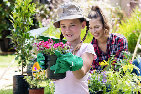Portrait of girl standing in garden with flower pot while mother gardening in backgroundの写真素材