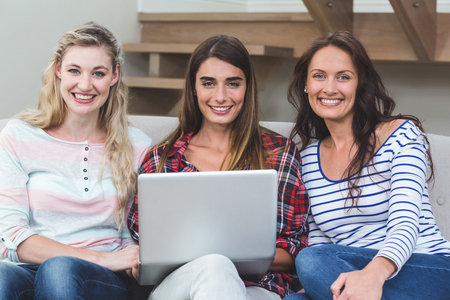 Portrait of friends sitting on sofa and using laptop at homeの写真素材