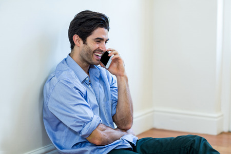 Man sitting on floor and talking on phone at homeの写真素材