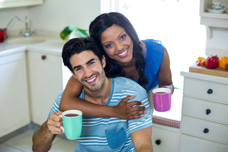 Portrait of young couple embracing while having coffee in kitchenの写真素材
