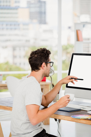 Young man holding coffee cup while working at his desk in the officeの写真素材