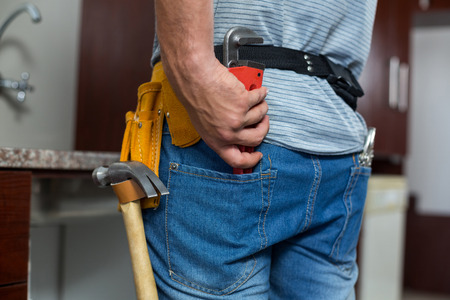 Rear view of man putting pipe wrench in pocket while standing at homeの写真素材