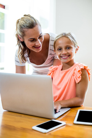 Mother teaching smiling daughter while using laptop at homeの写真素材
