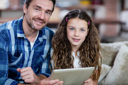 Portrait of father and daughter using digital tablet in living room at homeの写真素材