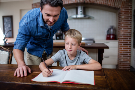 Father helping son with his homework in kitchen at homeの写真素材