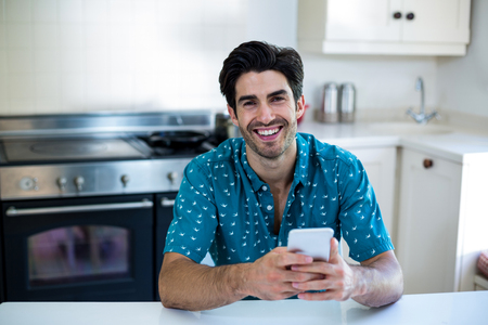 Portrait of young man using mobile phone in kitchen at homeの写真素材