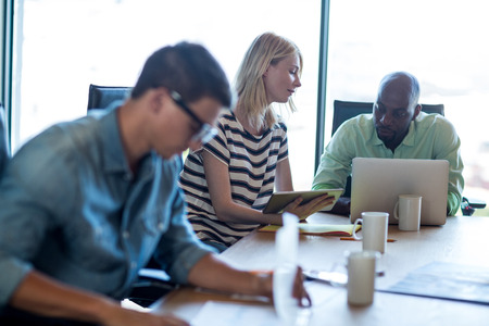 Colleagues interact at their desk using digital tablet and laptop in the office