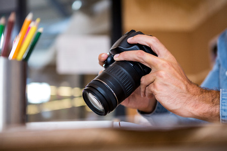 Man in office sitting at desk checking photo in cameraの写真素材