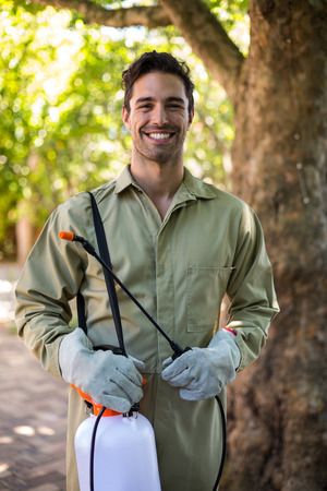 Portrait of happy worker with insecticide sprayer while standing by treeの写真素材