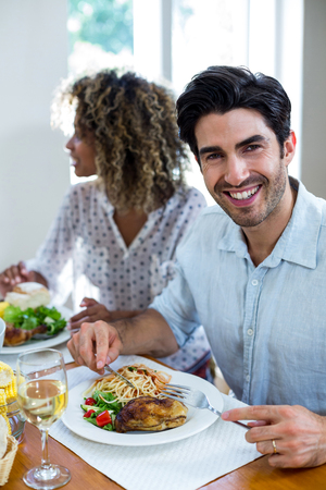 Portrait of happy man having meal and woman sitting in backgroundの写真素材