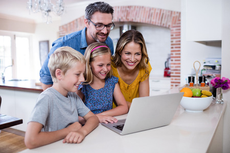 Parents and kids using laptop in kitchen at homeの写真素材