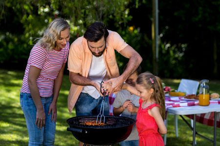 Father besides mother teaching children to barbecue food at yardの写真素材