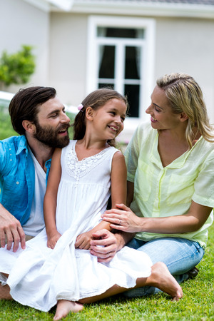 Happy girl with mother and father sitting on grass in yardの写真素材