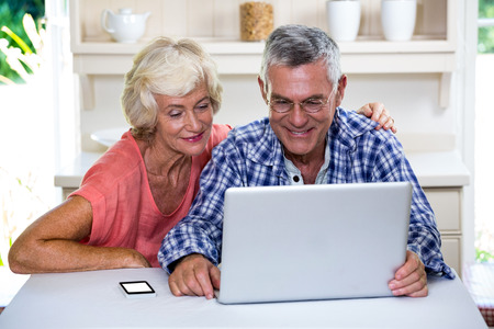 Happy senior couple using laptop in kitchen at home