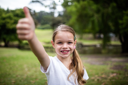 Portrait of a happy girl showing her thumbs up in the parkの写真素材