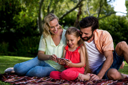 Close-up of happy parents with daughter looking at mobile phone in yardの写真素材