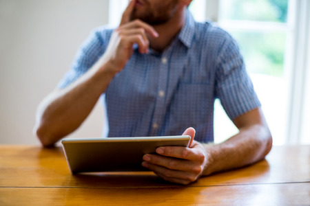 Midsection of man using digital tablet while sitting at tableの写真素材