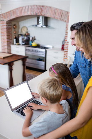 Parents and kids using laptop in kitchen at homeの写真素材