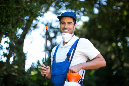 Portrait of happy insecticide worker against trees in back yardの写真素材