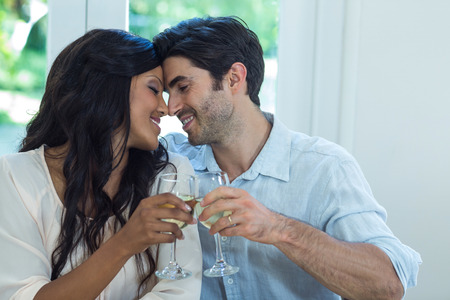 Young couple rubbing their nose while toasting wine at homeの写真素材