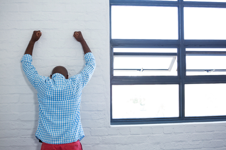 Rea view of upset man leaning against wall in officeの写真素材