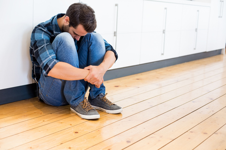 Tensed man sitting on wooden floor at homeの写真素材