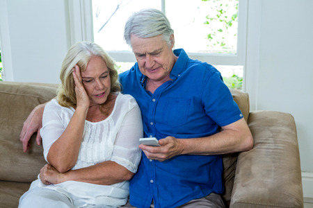 Senior couple using mobile phone while sitting in living room at homeの写真素材