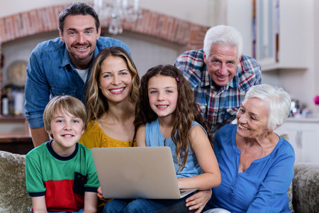 Multi-generation family sitting on sofa and using laptop at homeの写真素材