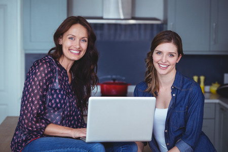 Two beautiful women using a laptop in kitchen at homeの写真素材