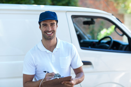 Portrait of happy delivery man with clipboard while standing by vanの写真素材