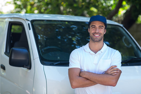 Portrait of cheerful delivery man with arms crossed while standing by vanの写真素材