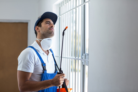 Thoughtful pest worker with sprayer looking up while standing at home
