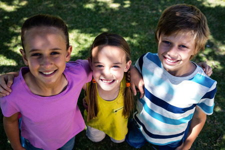 Portrait of happy children standing with arm around in park