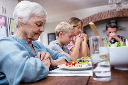 Multi-generation family praying before having meal at homeの写真素材