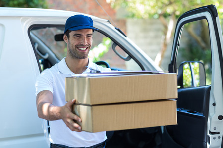 Smiling delivery man giving cardboard boxes while standing by vanの写真素材