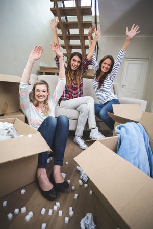 Portrait of friends sitting in their new house with arm raisedの写真素材