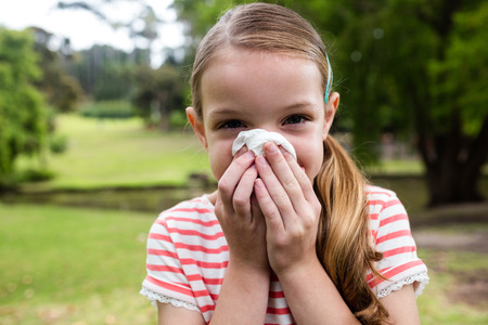 Sick girl covering her nose with tissue while sneezing in the parkの写真素材