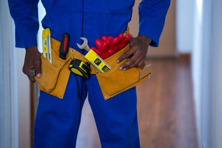 Mid section of handy man wearing tool belt at home