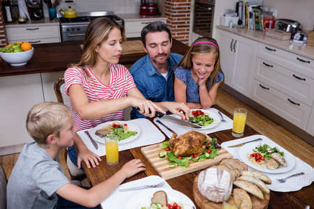 Woman cutting roasted turkey while having meal with his family at homeの写真素材