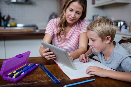 Mother using a digital tablet while helping son with his homework at home