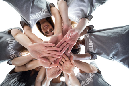 Happy volunteers in a circle putting their hands together against the skyの写真素材