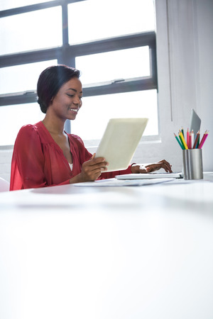 Woman using laptop and holding digital tablet in officeの写真素材