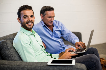 Colleagues sitting on a sofa discuss using laptop in the officeの写真素材