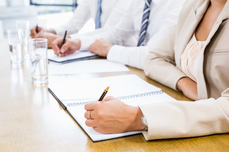 A Mid section of business colleagues is writing in a diary during a meeting