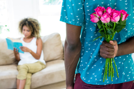 Man hiding flower from the woman in living roomの写真素材