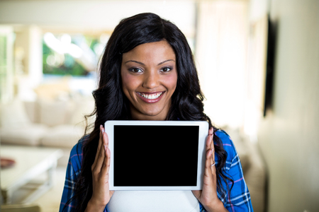 Portrait of young woman showing digital tablet at homeの写真素材