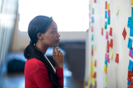 Young woman reading sticky notes on white board in the office