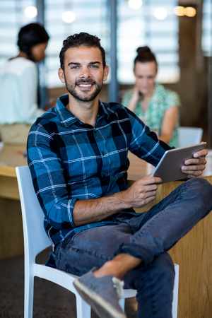 Portrait of young man holding digital tablet while colleague interacting in the backgroundの写真素材