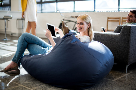 Portrait of young woman sitting on a bean bag holding digital tablet in the officeの写真素材