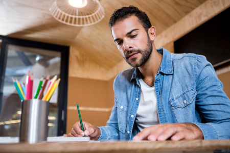 Man in office sitting at table and writing in a notepadの写真素材